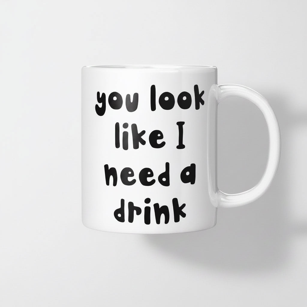 A white ceramic coffee mug with black text that reads 'you look like I need a drink'.