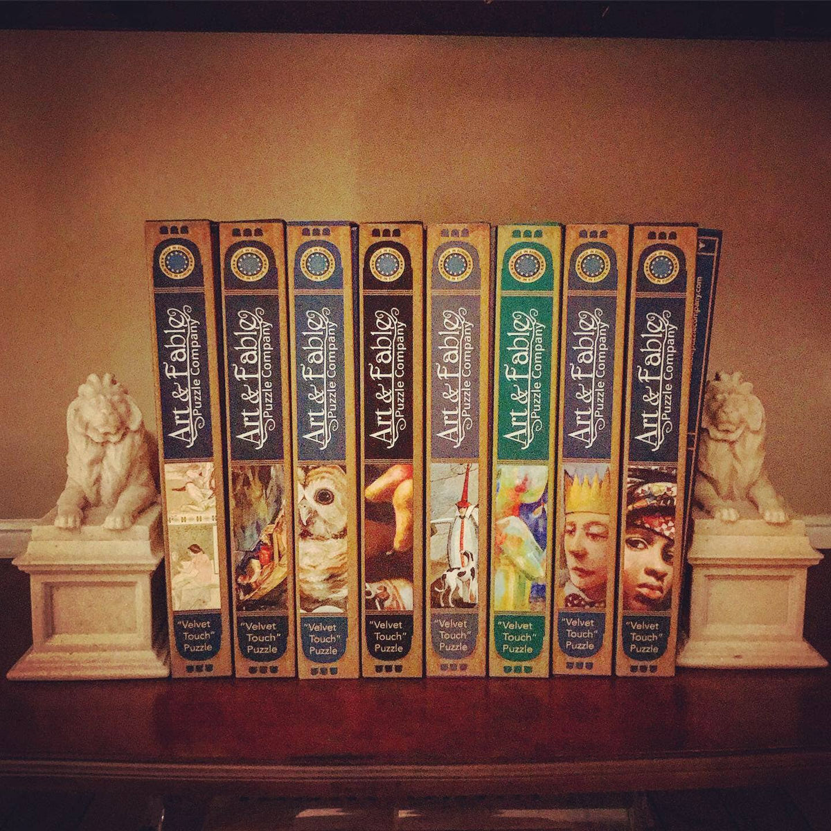 Row of 'Art & Fable' puzzle boxes on a shelf with decorative lion statues.