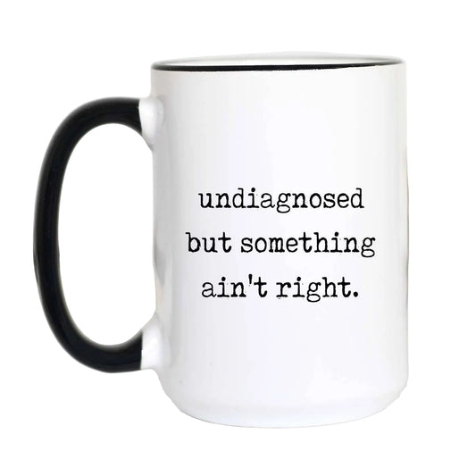 White mug with black handle and text 'undiagnosed but something ain't right.' on a white background.