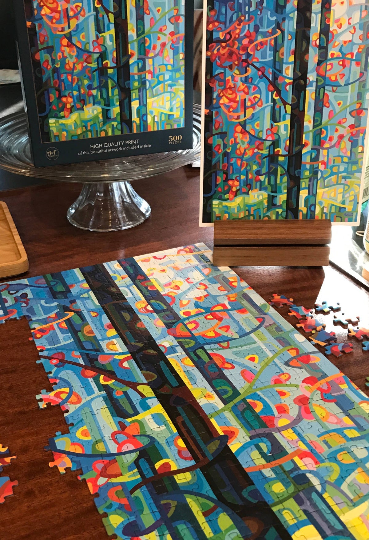 Colorful abstract artwork on a stand with a partially completed puzzle on a wooden surface.