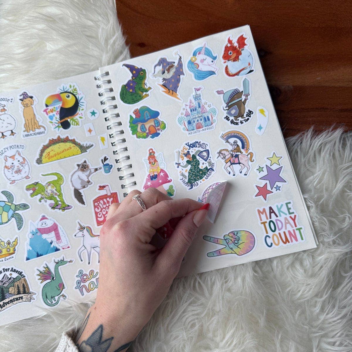 Sticker book with colorful stickers and a hand placing a sticker on a white surface.