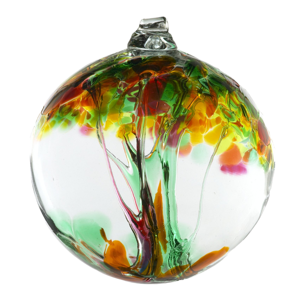 a transparent glass globe ornament sits in front of a white background. The ornament has strands of glass going from bottom to top like a tree trunk. Trunk widens at top and turns into branches ending as blotches of color imitating leaves. Colors include green, pink, orange, yellow, 