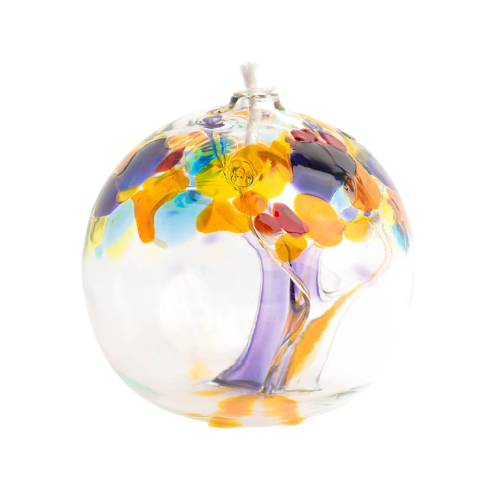 A blown glass oil lamp on a white background. The glass shows strands of glass inside and extending upward like the trunk of a tree. Spots of colored glass at the top of the glass imitates the look of leaves in colors of purple, turquoise, yellow, orange, and red.