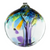 A round, blown glass ornament in colors of purple, blue, green and gold sits against a white background. Purple strands of glass begin at the base of the glove and extend up to the top,  imitating a tree trunk and expanding out like limbs of a tee. The limbs end at globs of color imitating the leaves on a tree.