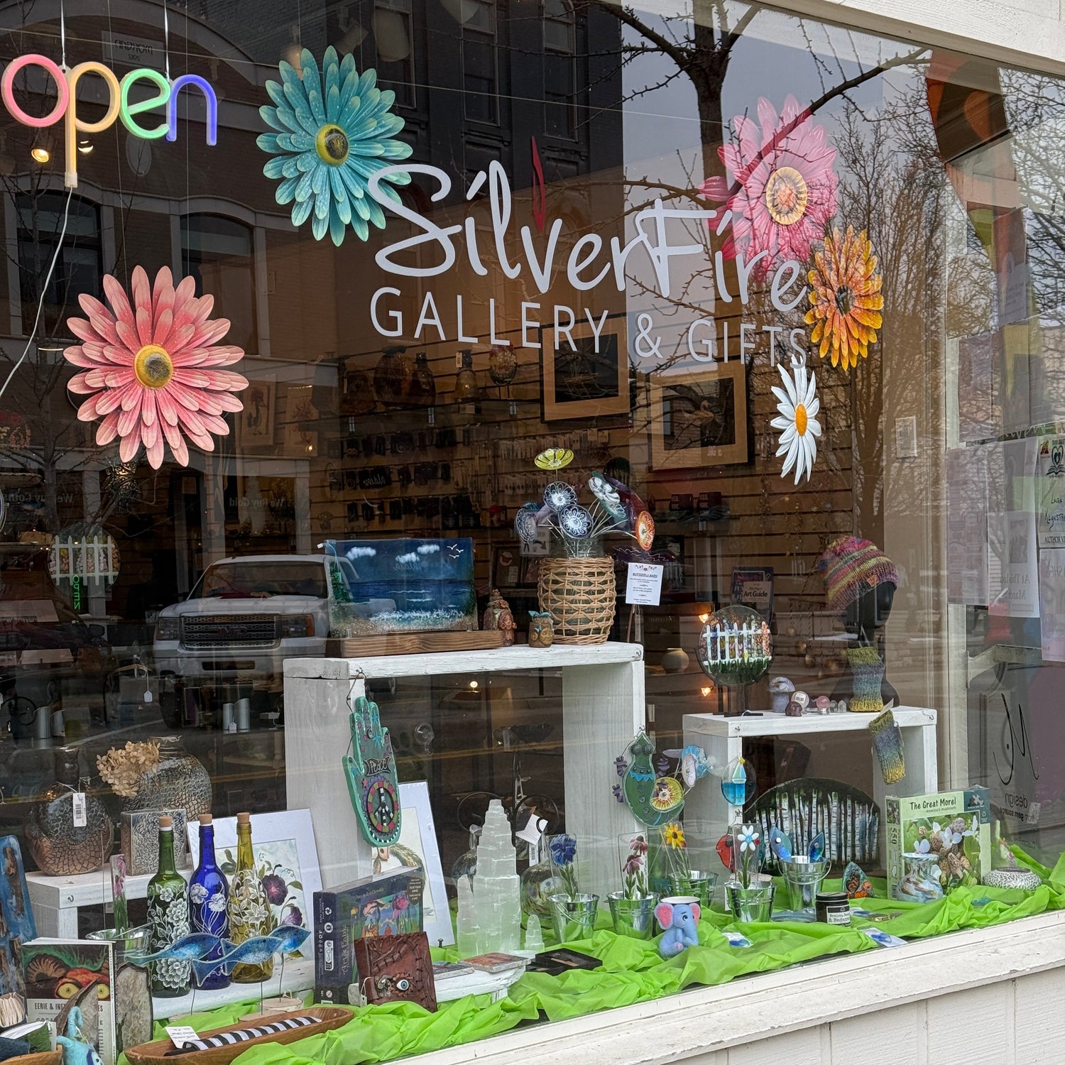 Storefront with 'SilverFire Gallery' sign and colorful flowers, reflecting urban street scene.