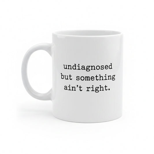 White mug with text 'undiagnosed but something ain't right' on a white background
