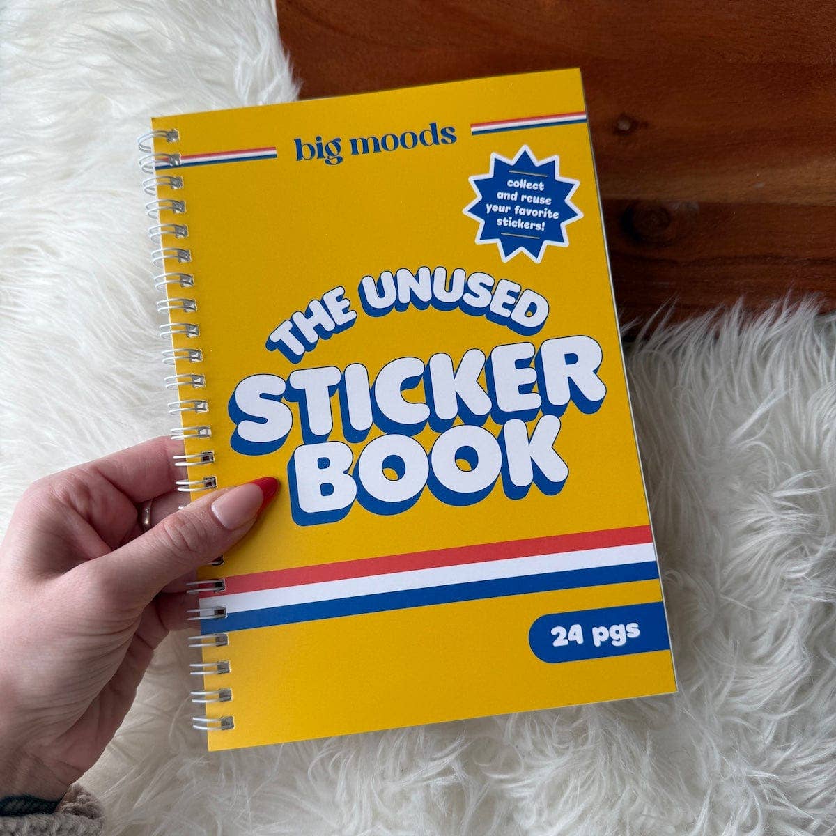 Yellow sticker book titled 'The Unused Sticker Book' held by a hand on a white fluffy surface.
