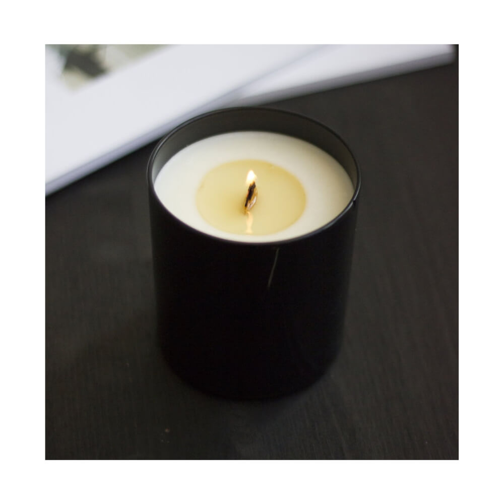 Candle with wood wick inside black canister with the words "fern + rain" in white lower case letters.